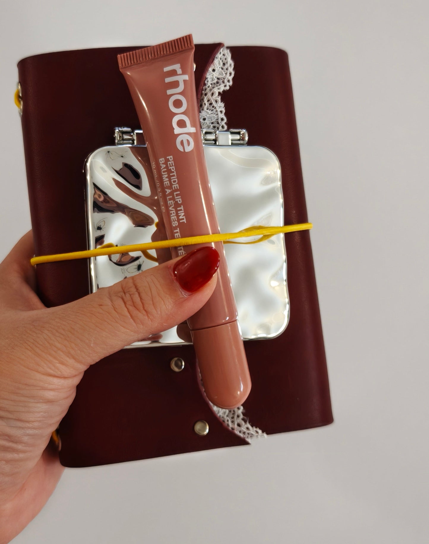 Hand holding a lip balm with burgundy leather journal against a neutral background